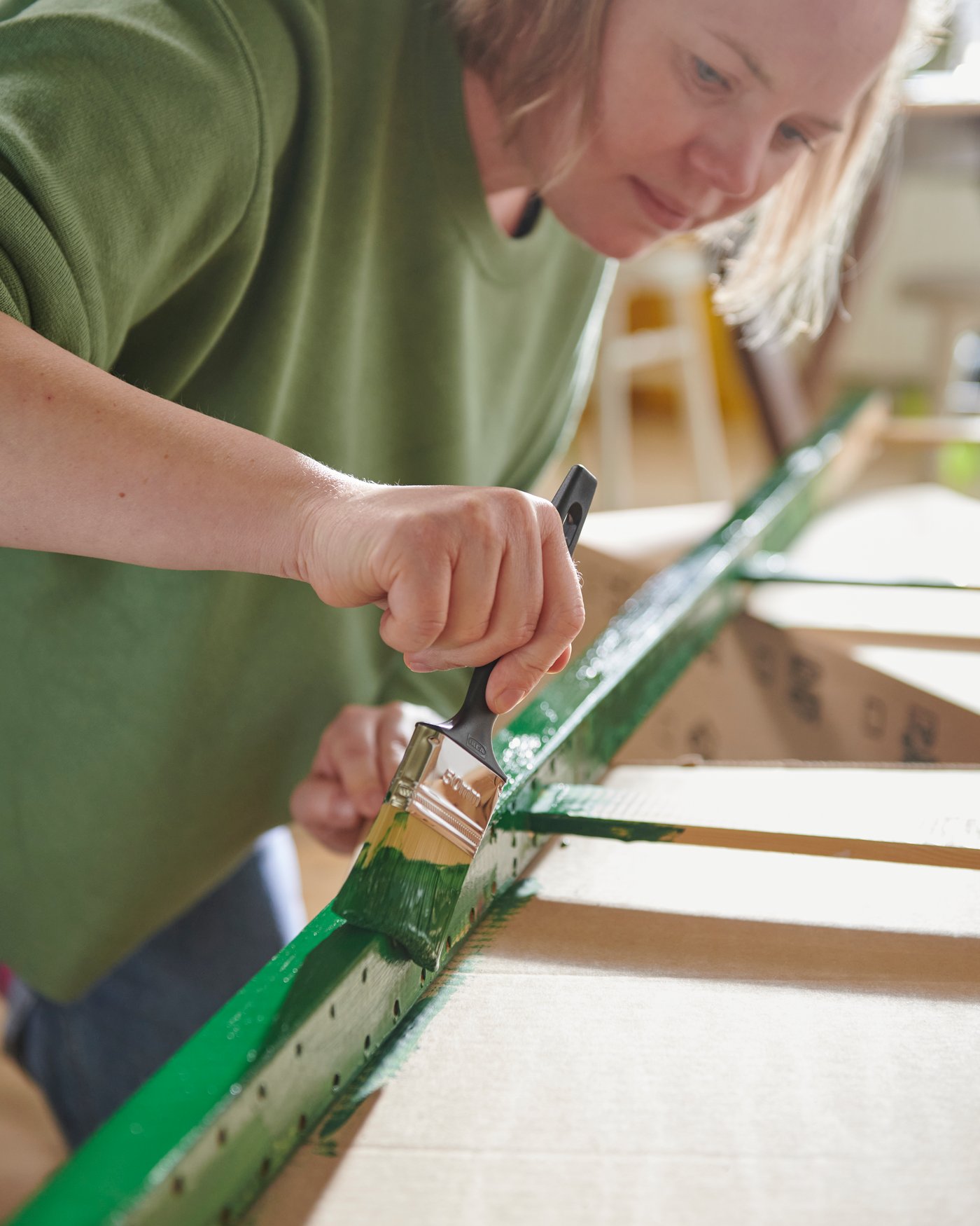 A person applies green paint to the edge of an IVAR shelving unit, showing that the solid wood can be painted.