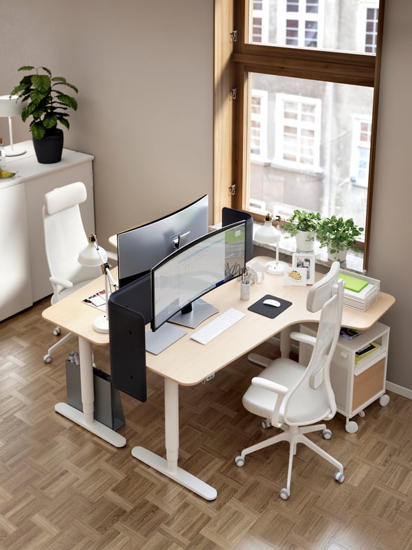 Two BEKANT corner desks facing each other beside a large window. Each desk has a JÄRVFJÄLLET chair and a storage unit.