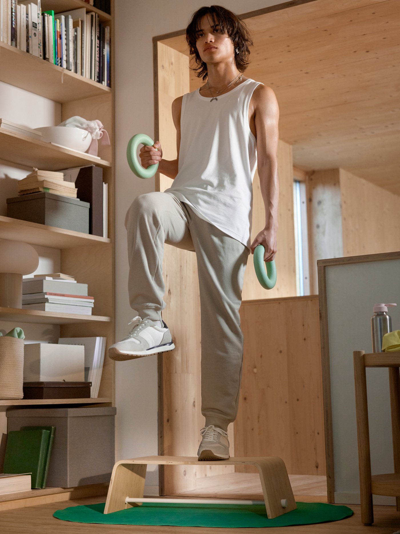 A man in workout wear is on the DAJLIEN step-up board, one knee up, holding the DAJLIEN training weights in his hands.