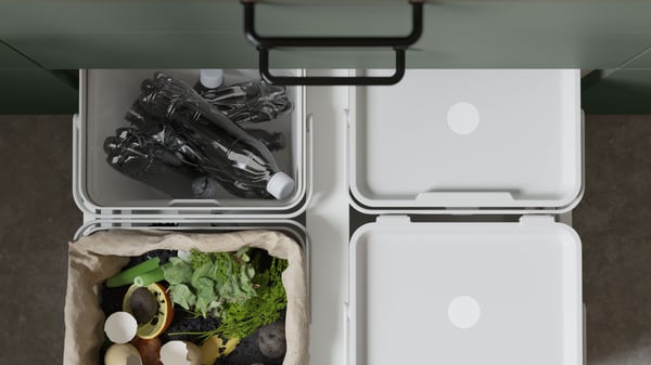 Källsorteringslådor i utdragen förvaring med plastflaskor och matavfall.