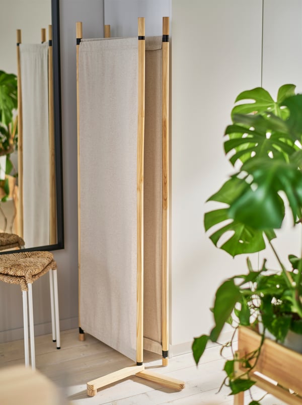 Separador de ambientes GLAMBERGET en madera sin tratar y textil beige plegado siguiente a los clósets PAX blancos.