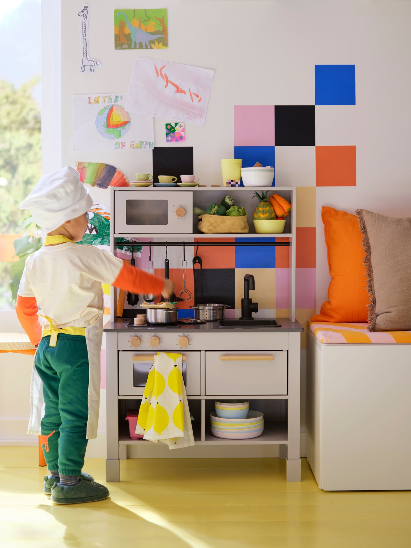 A child wearing a chef’s hat and an apron is standing by a grey SILLTRUT kitchen for children, stirring a pot on the hob.