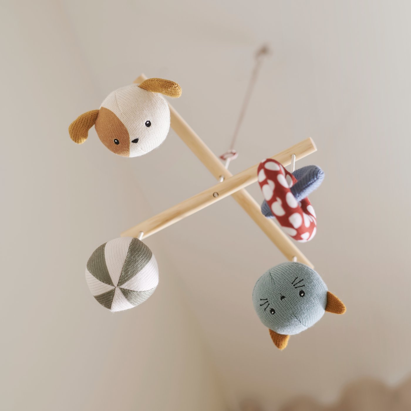 A GULDVÄVARE mobile with four hanging soft toys including a dog, a mushroom and a striped ball, on a wooden cross frame.