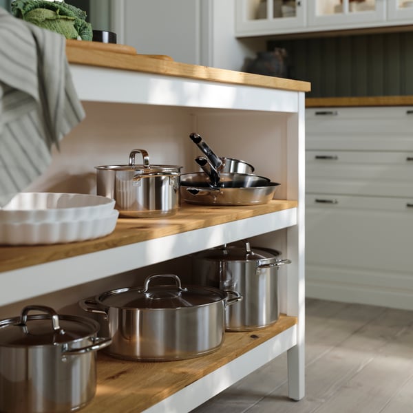 Ustensiles de cuisson IKEA 365+ en acier inoxydable sur les tablettes d’un îlot de cuisine TORNVIKEN en blanc cassé/chêne.