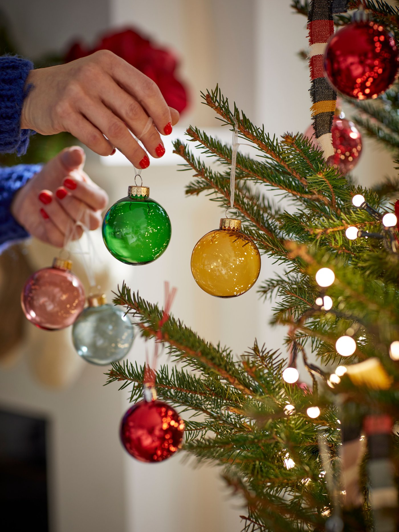 Una persona poniendo decoraciones a un árbol de navidad.