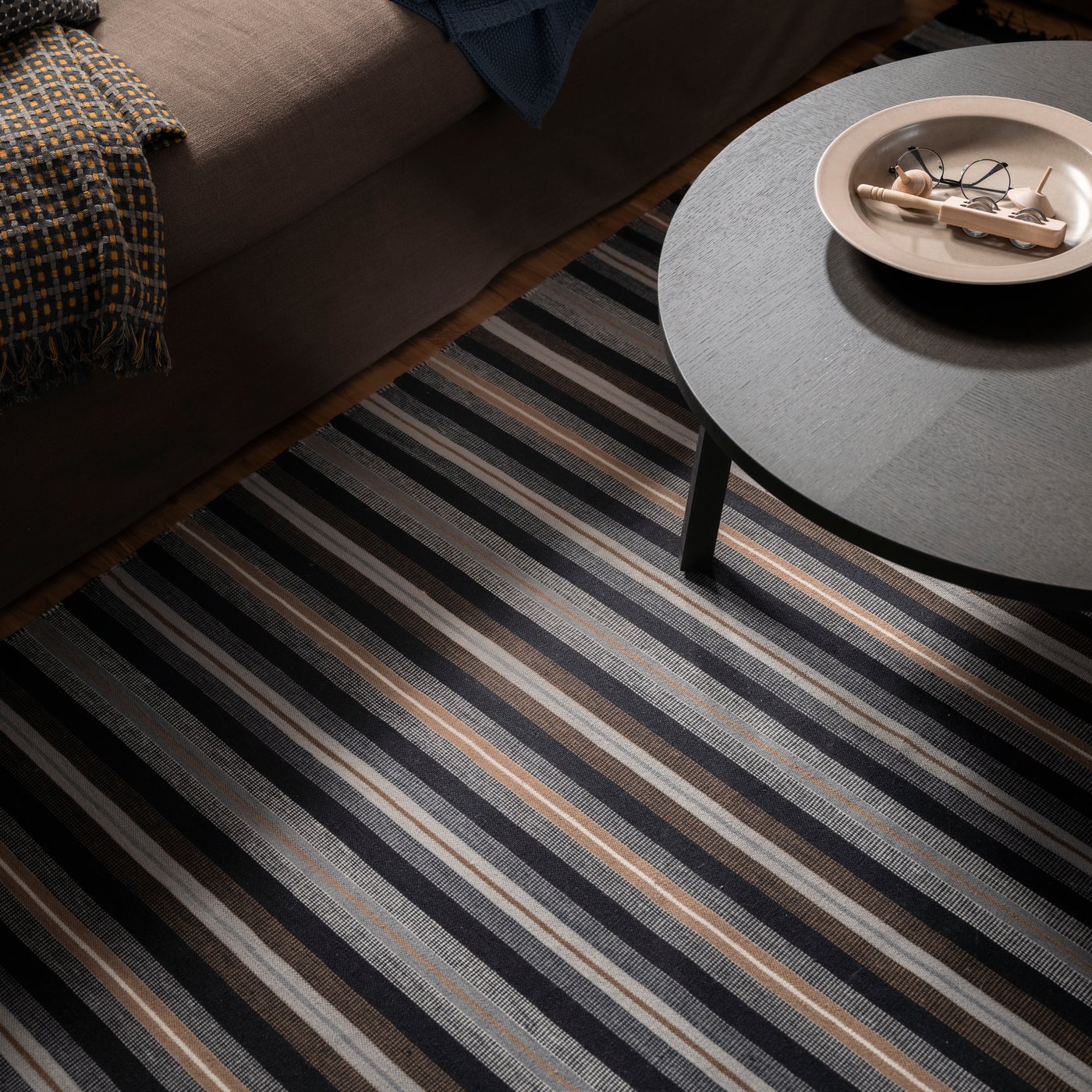 A STOCKHOLM 2025 serving bowl stands on a STOCKHOLM 2025 side table on a RÅVAROR flatwoven rug in a living room.
