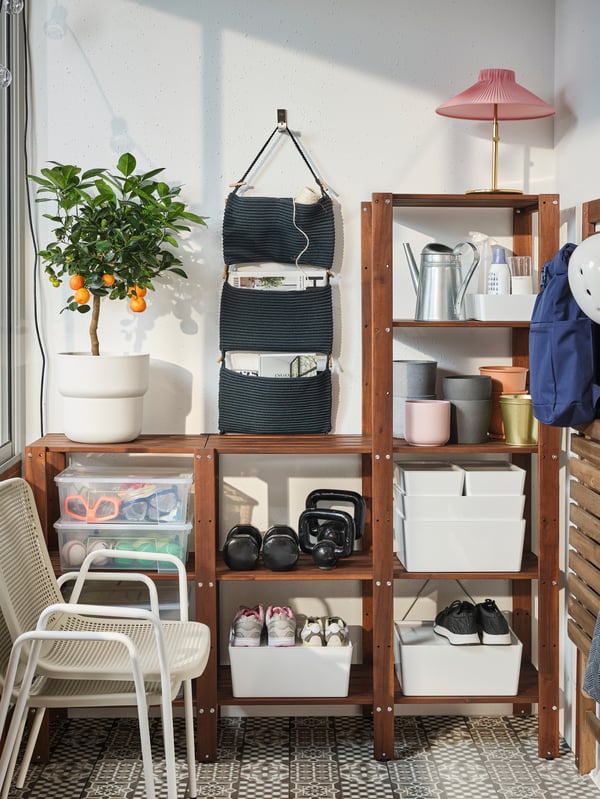 A spacious wooden shelving unit where storage boxes, plant pots and shoes are stored. Two chairs are stacked in front.