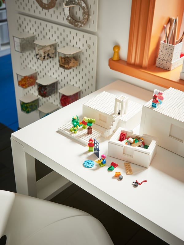 A white desk with white BYGGLEK LEGO® storage boxes with LEGO® figures in them and on the lids.