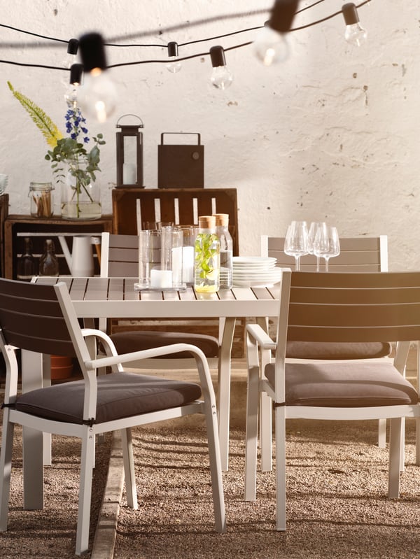A row of chairs and small tables in the process of being set for a party under a decorated pergola in a courtyard.