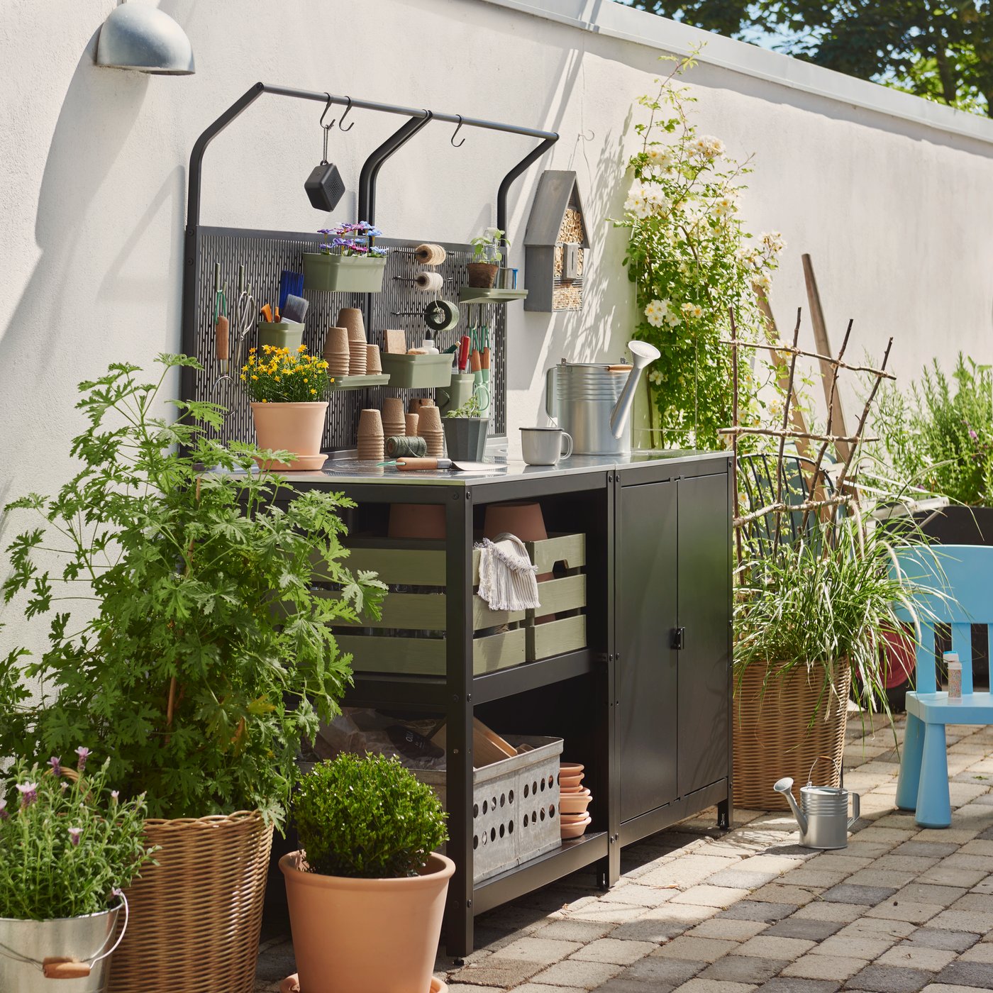 Eine schwarze und rostfreie GRILLSKÄR Kücheninsel steht in einem Garten mit grünen Pflanzen, Töpfen und Gartengeräten darauf.