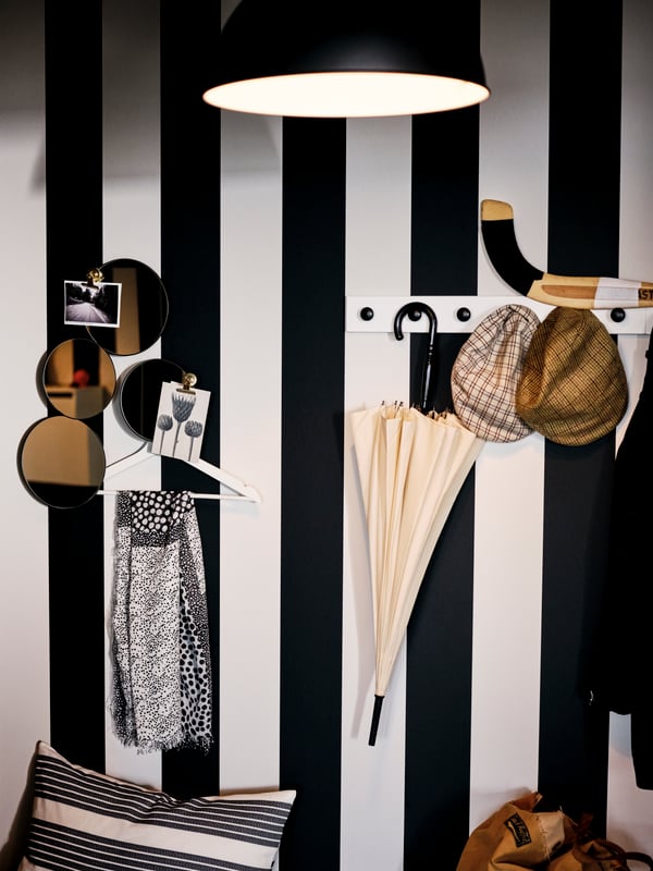 Plusieurs articles sont accrochés sur le mur avec des rayures larges noires et blanches. Certains sont suspendus aux crochets ENERYDA noirs sur une patère LURT blanchie.