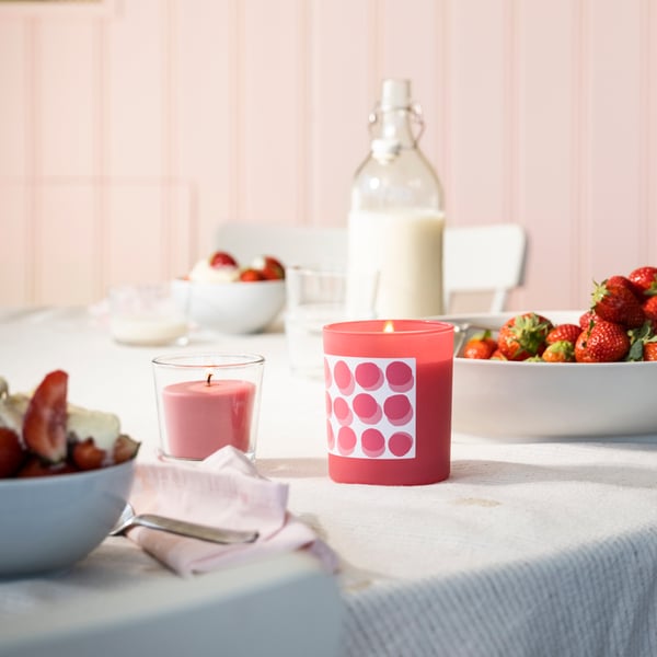 A Strawberry/bright pink BLODBOK scented candle in glass on a dining table.