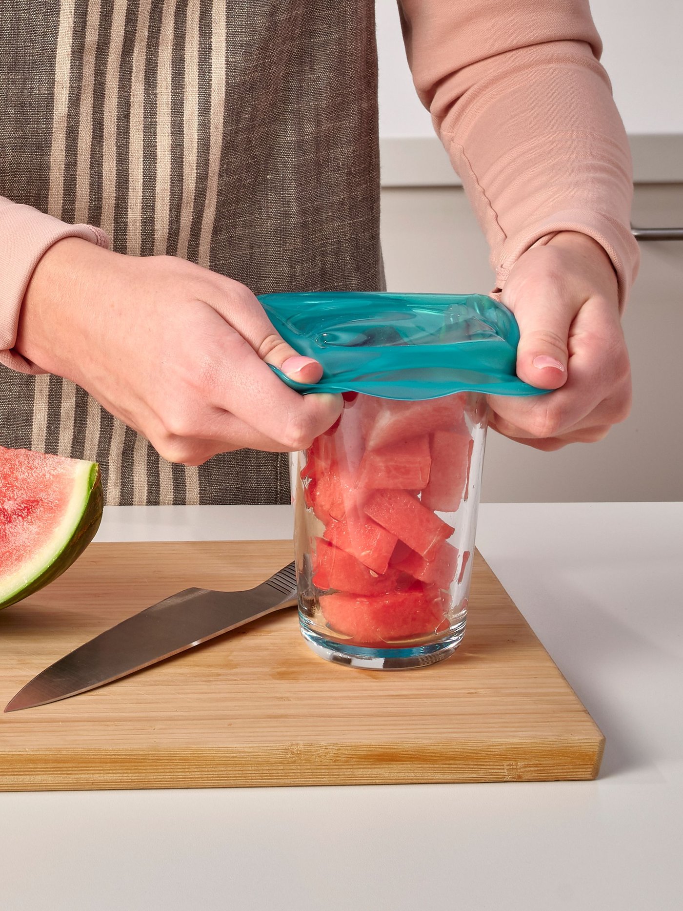 Una persona tapa un bowl con fruta con una tapa plástica reusable.