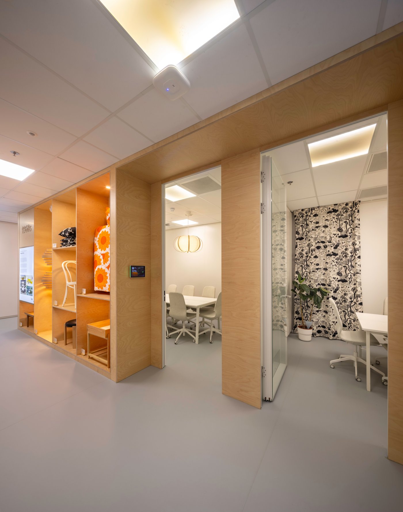 Un couloir de bureau avec trois salles de réunion distinctes, chacune avec son propre intérieur : une alcôve orange, une salle de réunion blanche et un espace vitré avec papier peint botanique.