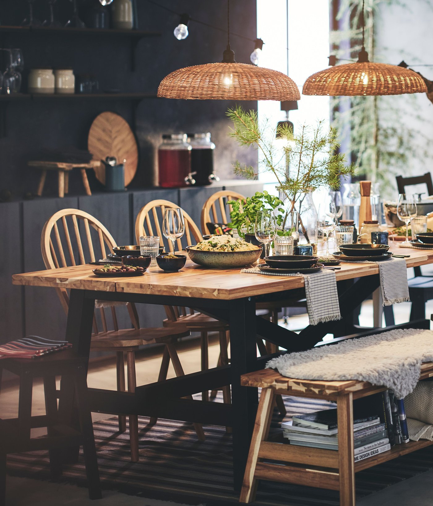 A cozy dining area with SKOGSTA wooden table surrounded by chairs, decorative plants, and warm hanging lights.