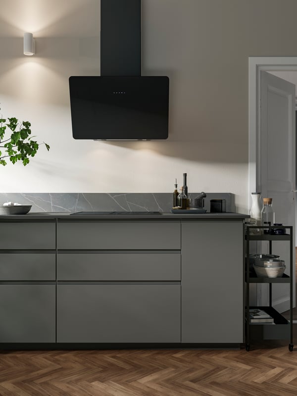 A black HÖGKLASSIG induction hob and a black wall-mounted INSMAKARE extractor hood are placed in a dark grey VOXTORP kitchen.