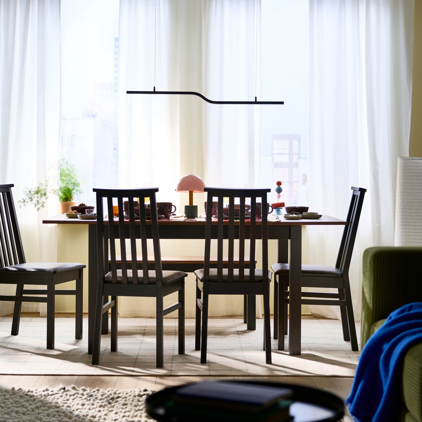 A dining area featuring an ÅLHULT extendable table surrounded by four chairs and accented by a BACKSTÖRN LED pendant lamp.