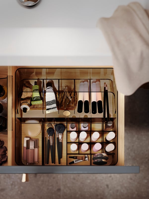 Cassetto aperto con un contenitore a scomparti VISSLAÅN grigio in cui sono organizzati diversi cosmetici e prodotti per il bagno.