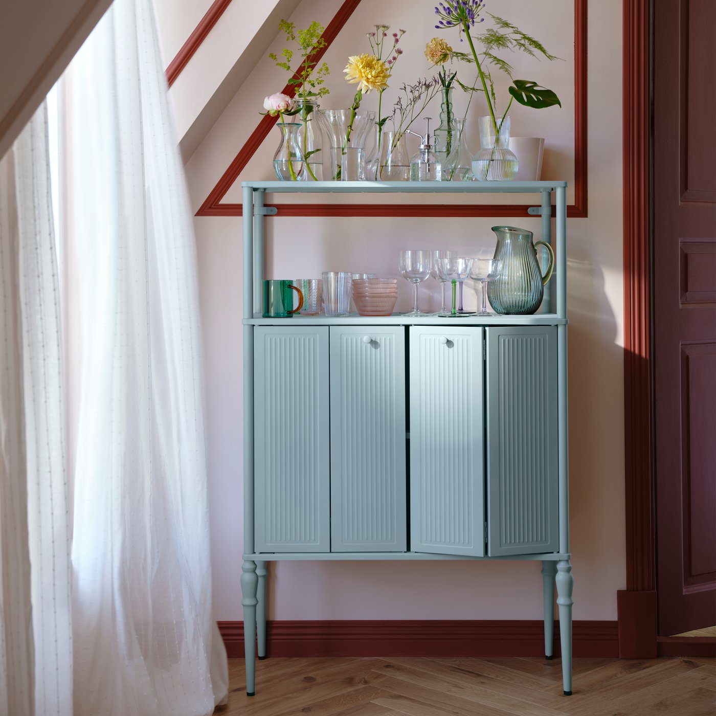 Et lyseblåt SÅGMÄSTARE skab med glas og krukker ovenpå, elegant placeret i et stilfuldt interiør.