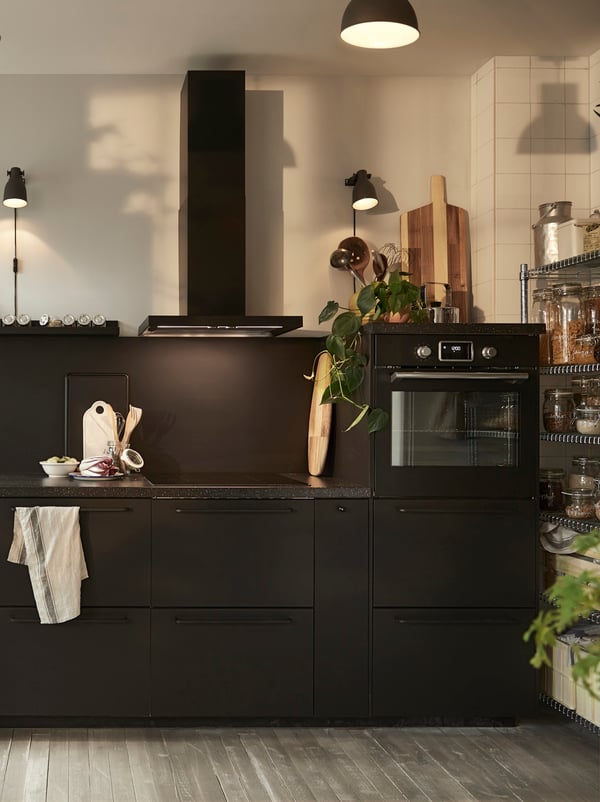 A black kitchen with a black extractor hood, a black built-in oven and a black mineral effect worktop.