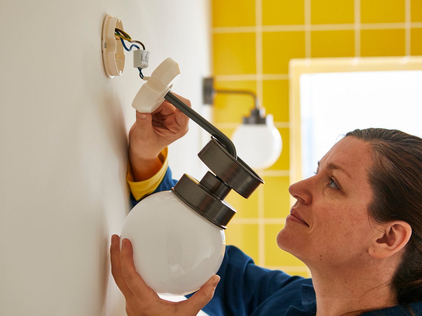 Een glimlachende IKEA medewerker houdt een verlichtingsarmatuur vast in een badkamer.