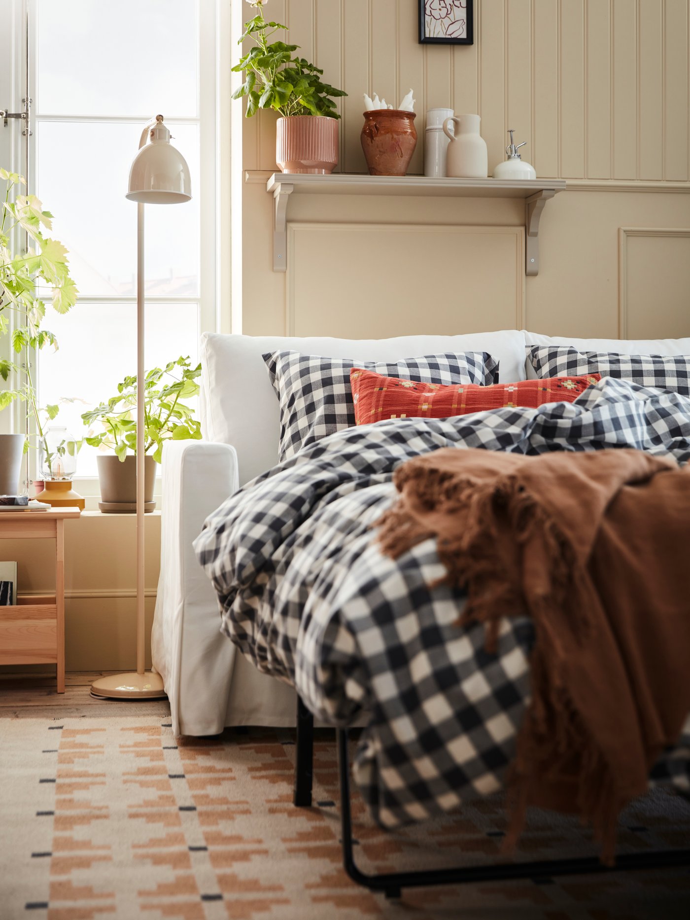 A white HYLTARP 2-seat sofa-bed, configured as a bed, with EXTANDVINGE bed linen stands on a TELEGRAFLINJE rug.