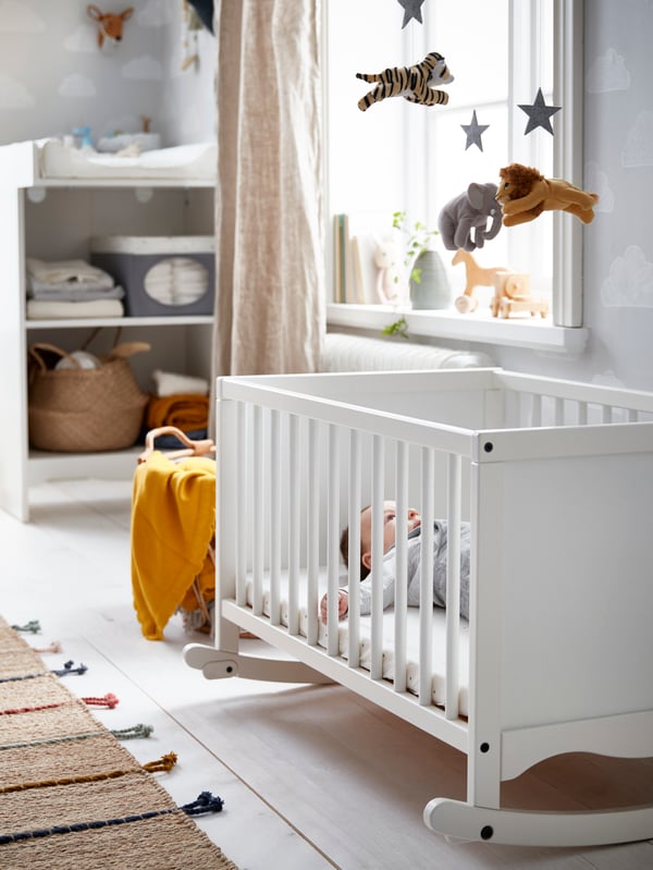 Beba leži u IKEA SOLGUL krevecu u sobi s belim drvenim podnim oblogama i prirodnim tekstilnim tepihom i korpom.