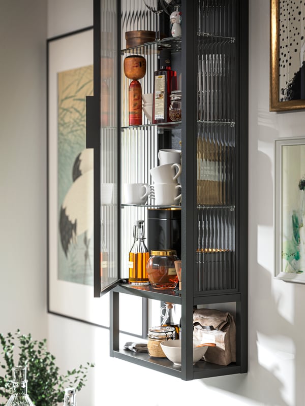 A close-up of an open MOSSJÖN wall cabinet with shelves and glass door with some cups and bottles in it.