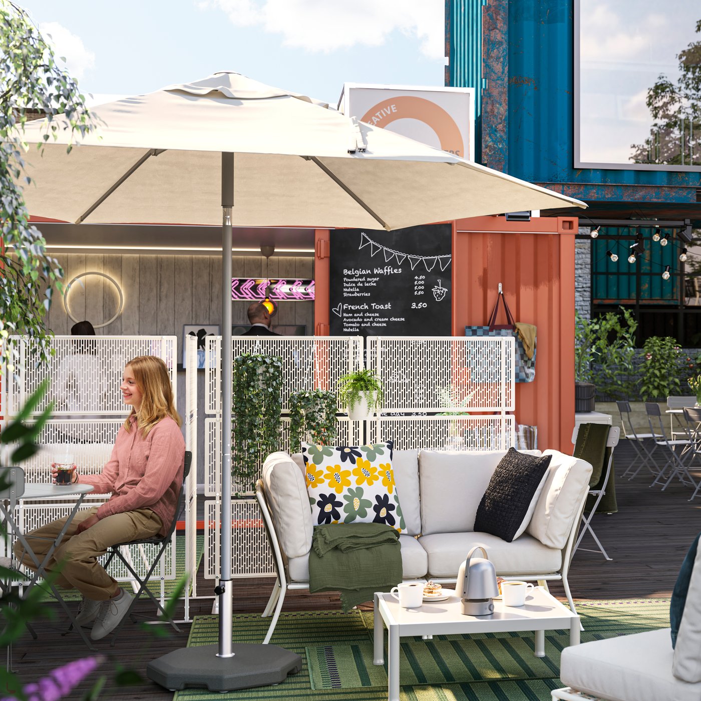 The sun is shining on an outdoor lounging area in a container village. People are socialising around grey SUNDSÖ tables.