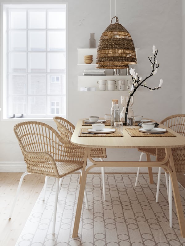 An open dining room with light wood dining table in neutral tones, Wicker and metal chairs. On top ceramic and metal homewares are combined for a modern organic look an feel.
