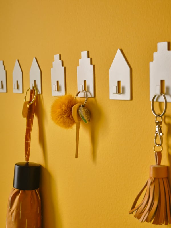 A wall section with multiple house-shaped TIPPVAGN self-adhesive hooks, arranged side by side in a row.