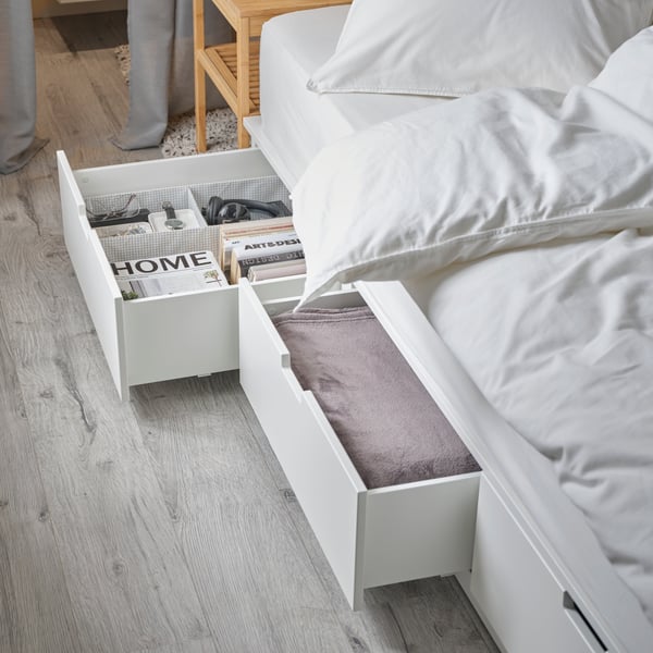 En NORDLI sängstomme med förvaring bäddad med vita sängkläder. Två av lådorna är utdragna så att man delvis ser innehållet.