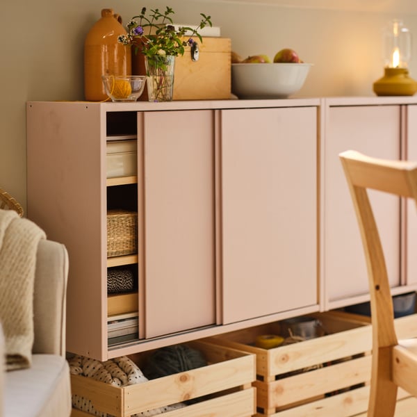 Two IVAR cabinets with sliding doors painted pink on a wall with a bowl and vases on top and KNAGGLIG boxes underneath.