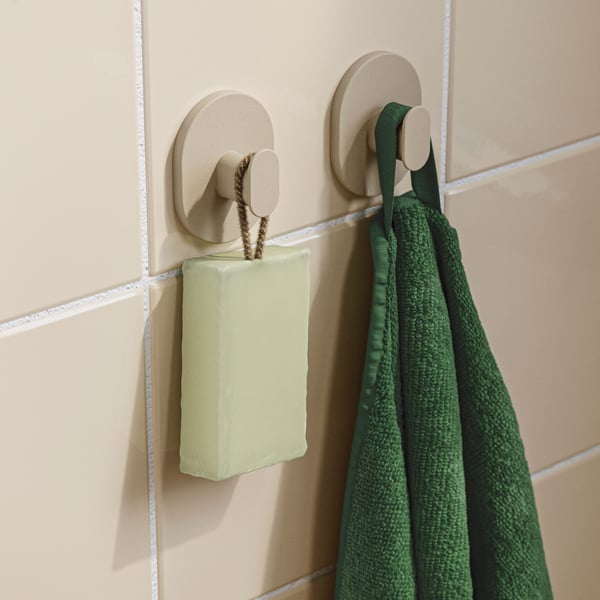 Su una parete piastrellata di un bagno, primo piano di un set di 2 ganci grigio-beige a cui sono appesi un asciugamano verde e una saponetta verde menta.