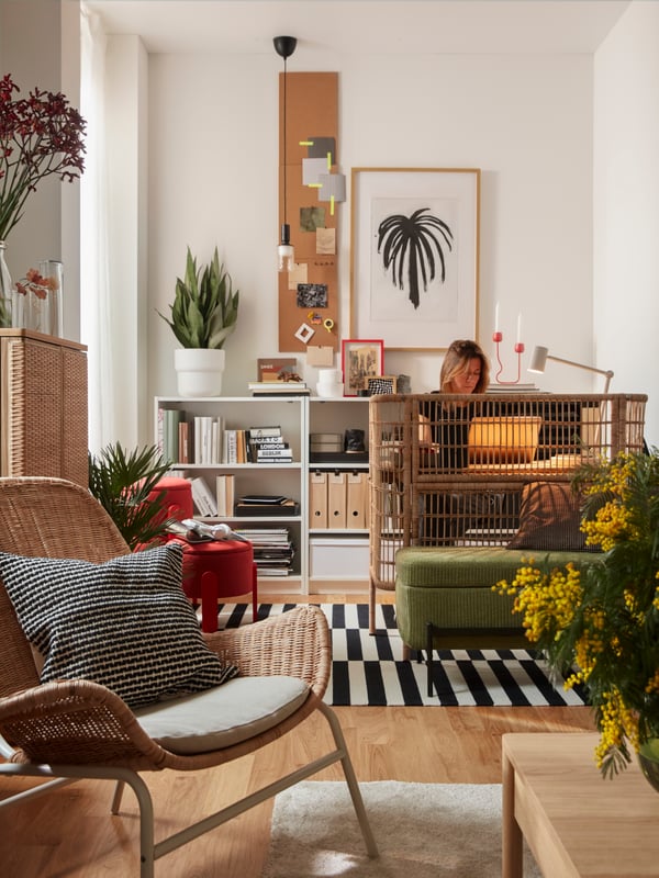 Es ist ein Wohnzimmer mit verschiedenen FRYKSÅS Möbelstücken zu sehen; darunter ein Schreibtisch, an dem eine Person mit Laptop sitzt.