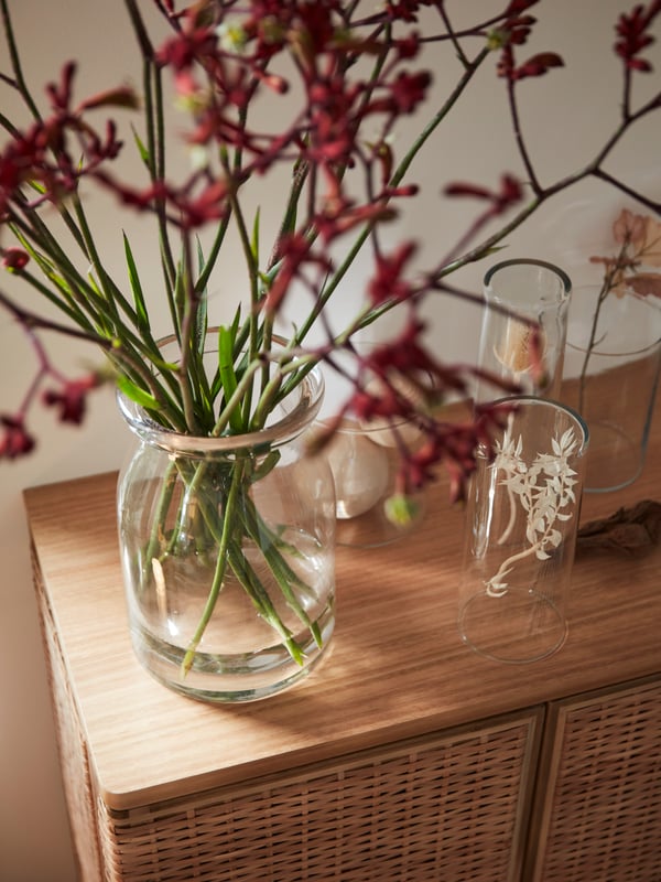Auf der Oberseite eines FRYKSÅS Schranks sind Blumenarrangements in BEGÄRLIG und ZYLINDER Vasen zu sehen.