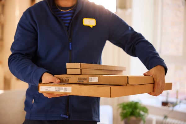 IKEA-työntekijä kantaa neljää litteätä pahvilaatikkoa käsissään.