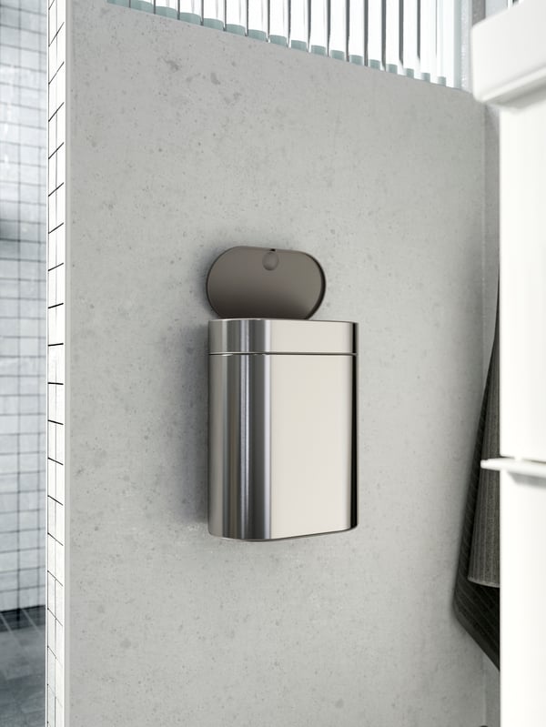 An open BROGRUND touch top bin in stainless steel, mounted on a grey wall with marble effect.