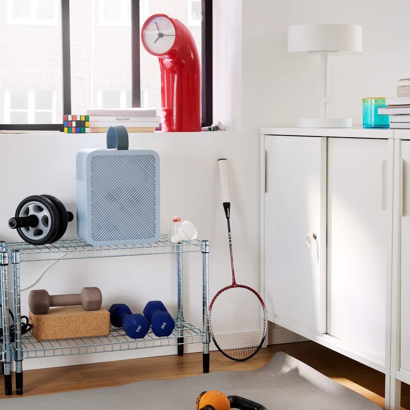 A gym corner features a blue UPPÅTVIND air purifier on a shelf, next to weights and a yoga mat on the floor.