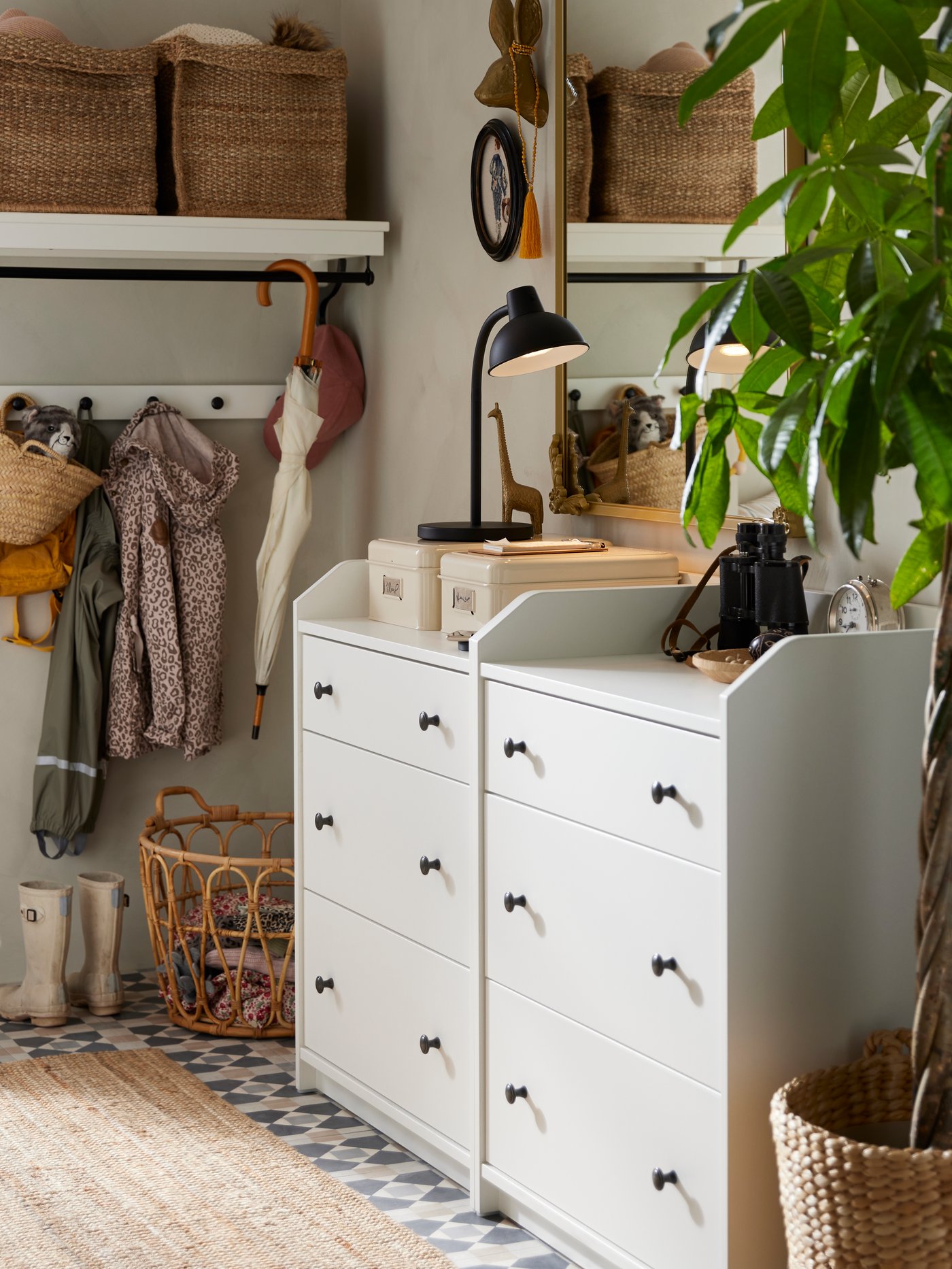 Una habitación con dos cómodas HEMNES de tres cajones ordenadas una al lado de la otra. En el fondo una repisa con canastas y debajo un colgador con prendas de ropa colgando.