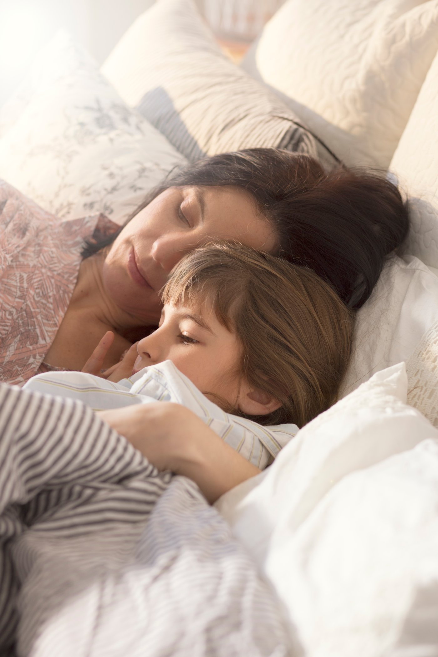 Une femme avec un enfant dans les bras dans un lit aux draps clairs.