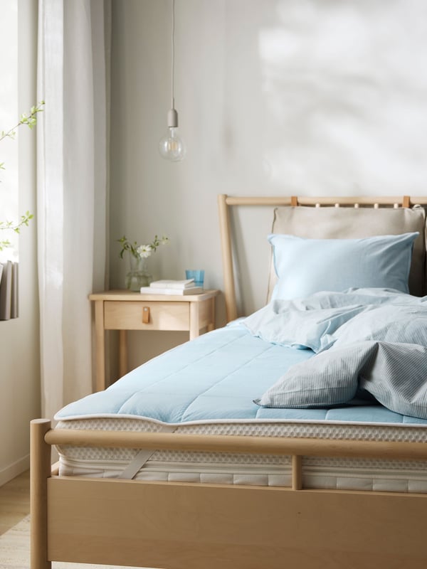Close-up of foot end of a bed in brushed oak with a matching bedside table. Cooling mattress protector on the bed.