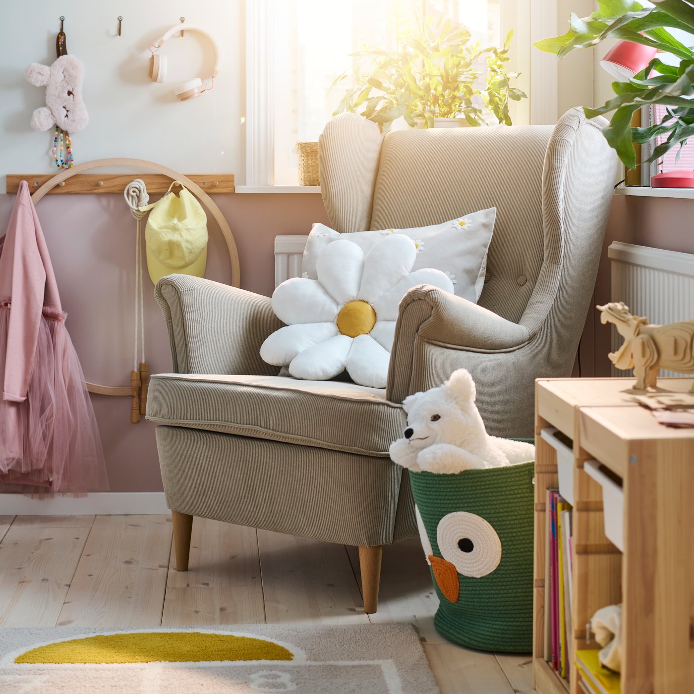 Ein beiger STRANDMON Flügelsessel in einem hellen Kinderzimmer mit einem weißen, blumenförmigen SKOGSDUVA Kissen darauf.