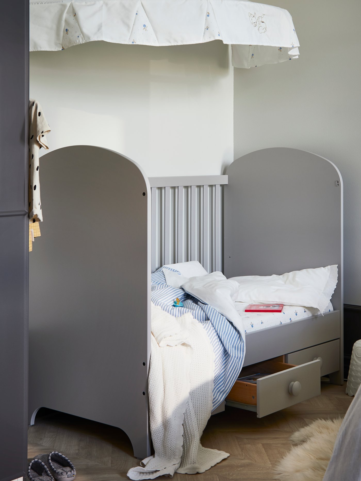 A GONATT cot that has one side removed and has one drawer pulled out stands in a corner under a RÖDHAKE canopy.