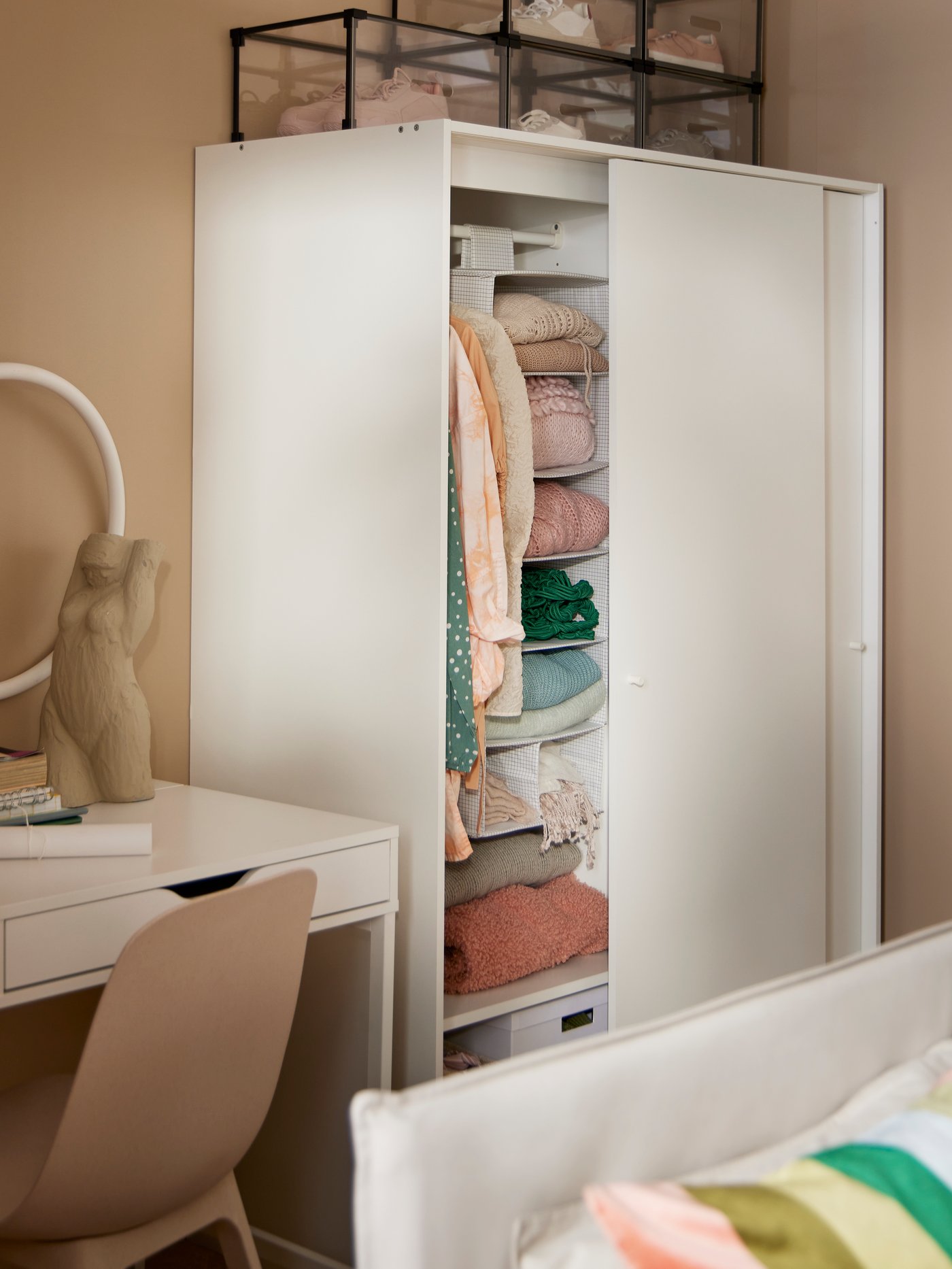 Es ist ein weisser Kleiderschrank in einem Schlafzimmer mit Schreibtisch und Bett zu sehen.
