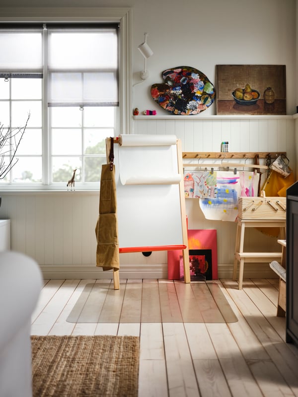 A wooden-floor room with an arts-and-crafts corner with a MÅLA softwood easel, a PERJOHAN pine stool with storage, and more.