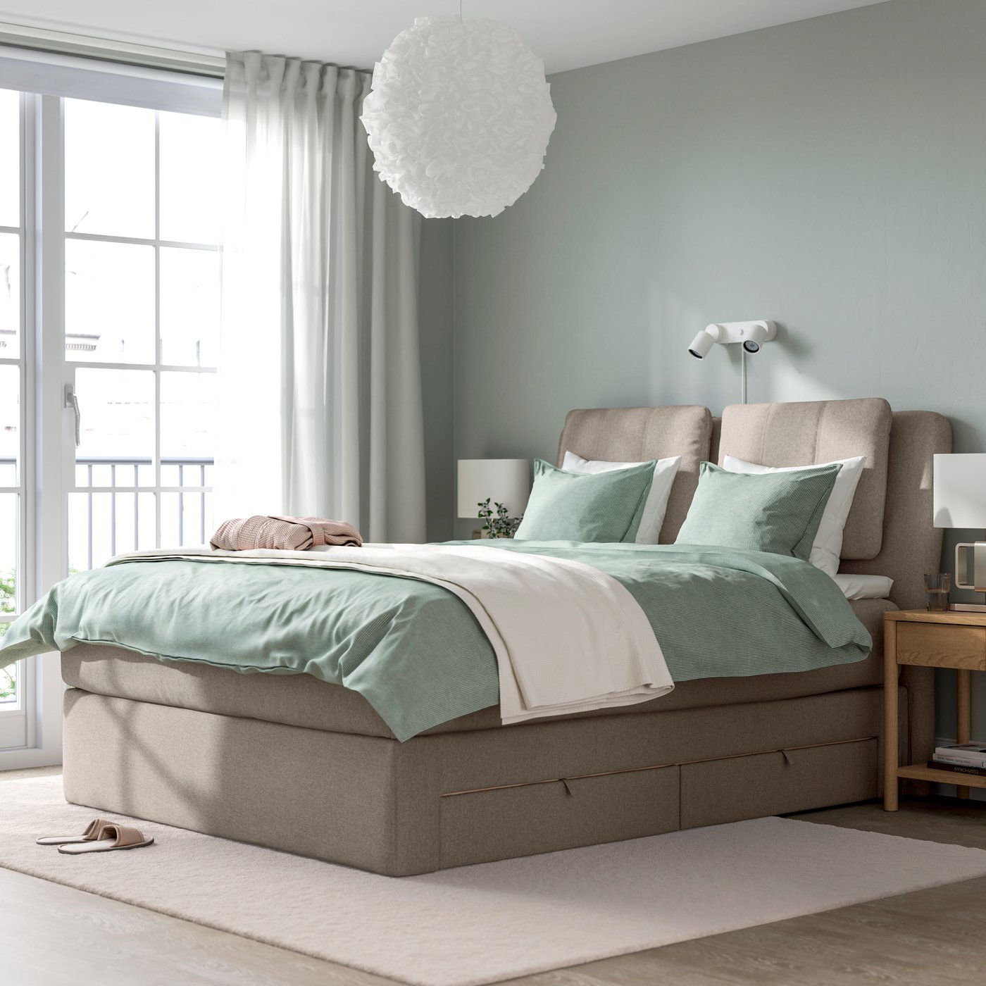 Ein graues LILLFJÄLLET Boxspringbett mit Bettwäsche in MIntdrün und naturfarbenem Plaid in einem Schlafzimmer.