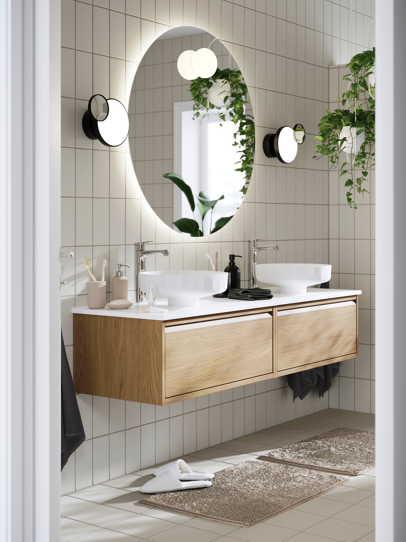 Modern bathroom with dual sinks on an oak-finished ÄNGSJÖN wash-stand with drawers, round mirror, and hanging plants.