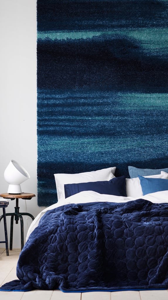 Dormitorio con ropa de cama azul y una alfombra azul colgada sobre la pared.