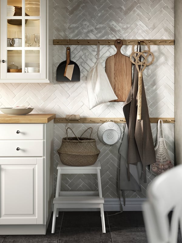 A kitchen with HÖVOLM racks with 6 knobs with an ARTISTISK chopping board in oak and a GEMAK colander in off-white hanging.